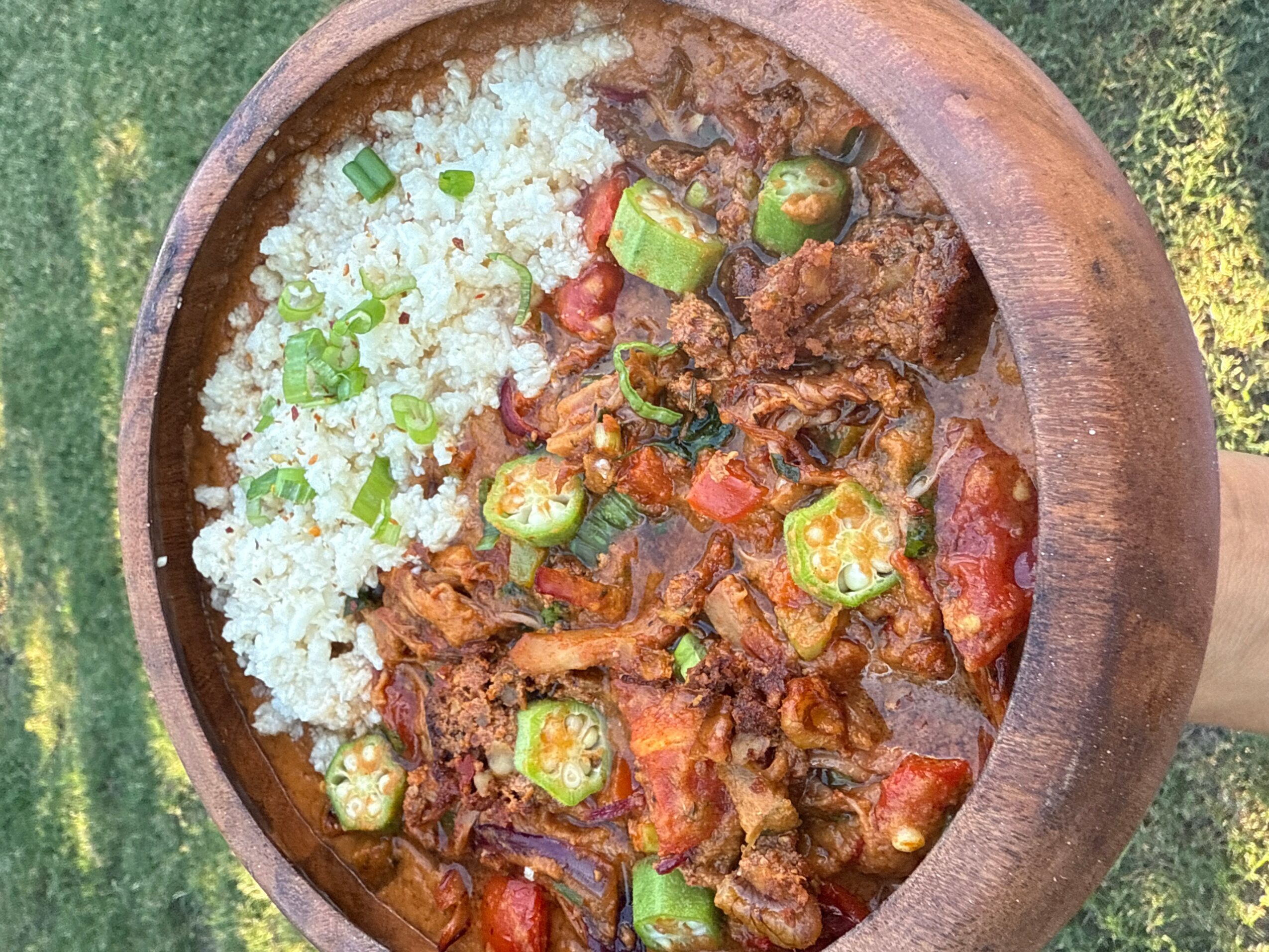 Stew with okra, tomatoes, and meat served in a wooden bowl, with rice on the side.