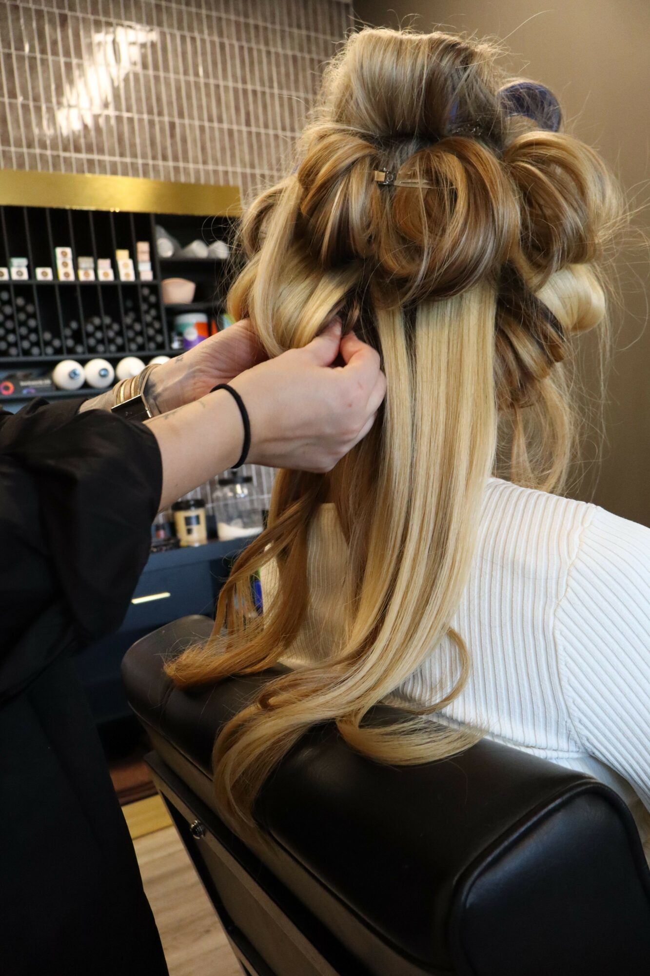 Person with long, curled hair working at a salon station with hair products in the background.