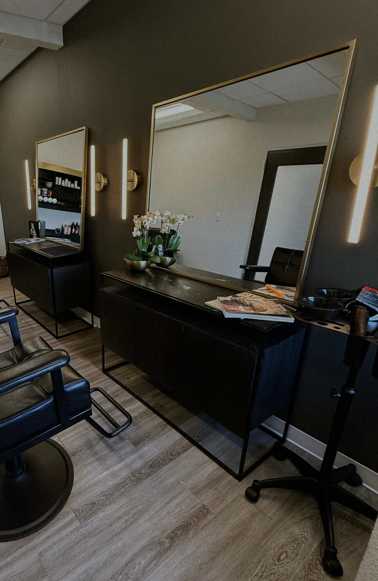 Salon with a large mirror, black furniture, a TV, and a chair, with a vase of flowers on the table.