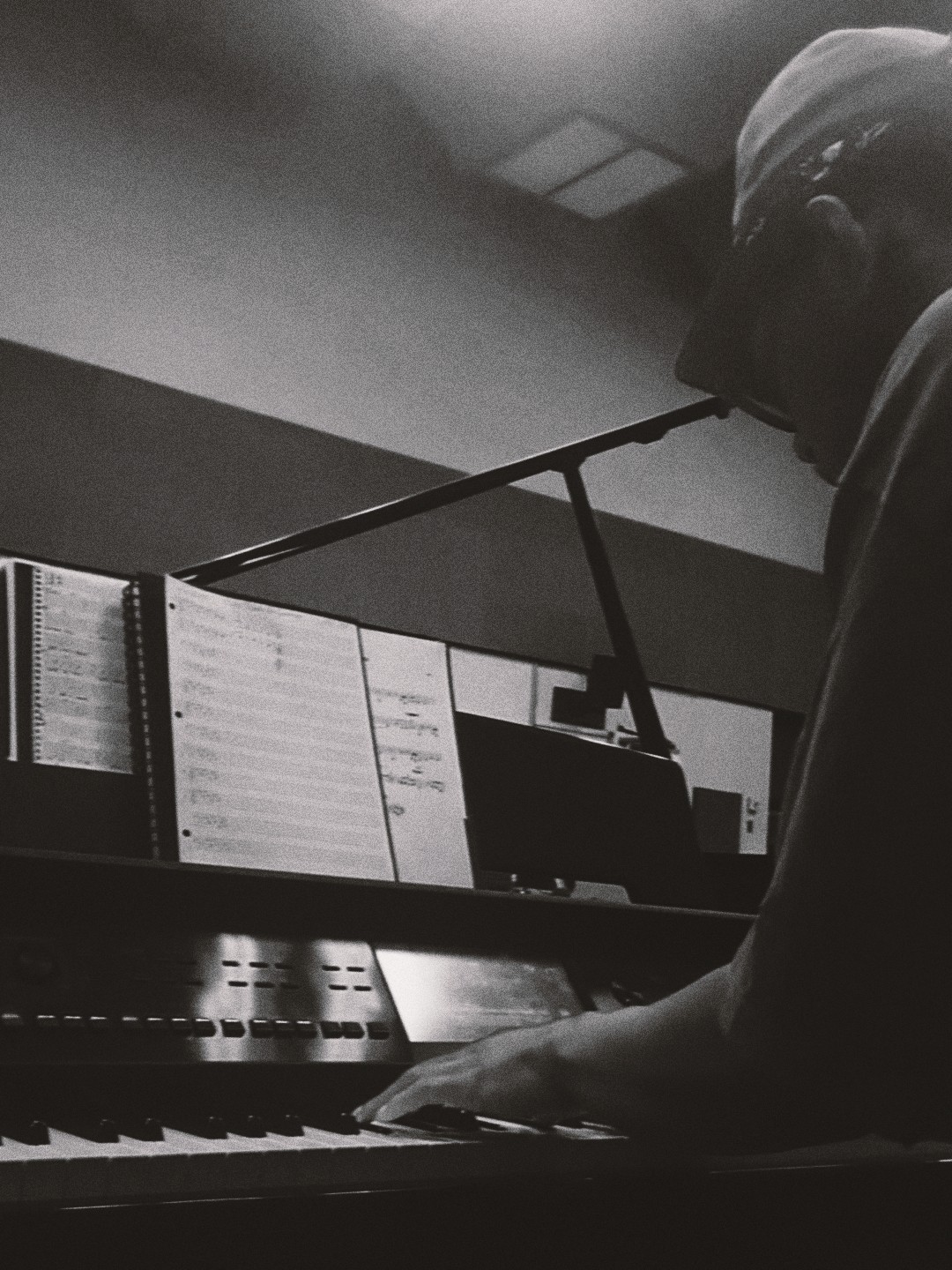 Person playing piano, reading sheet music, in a dimly lit room, with a microphone nearby.