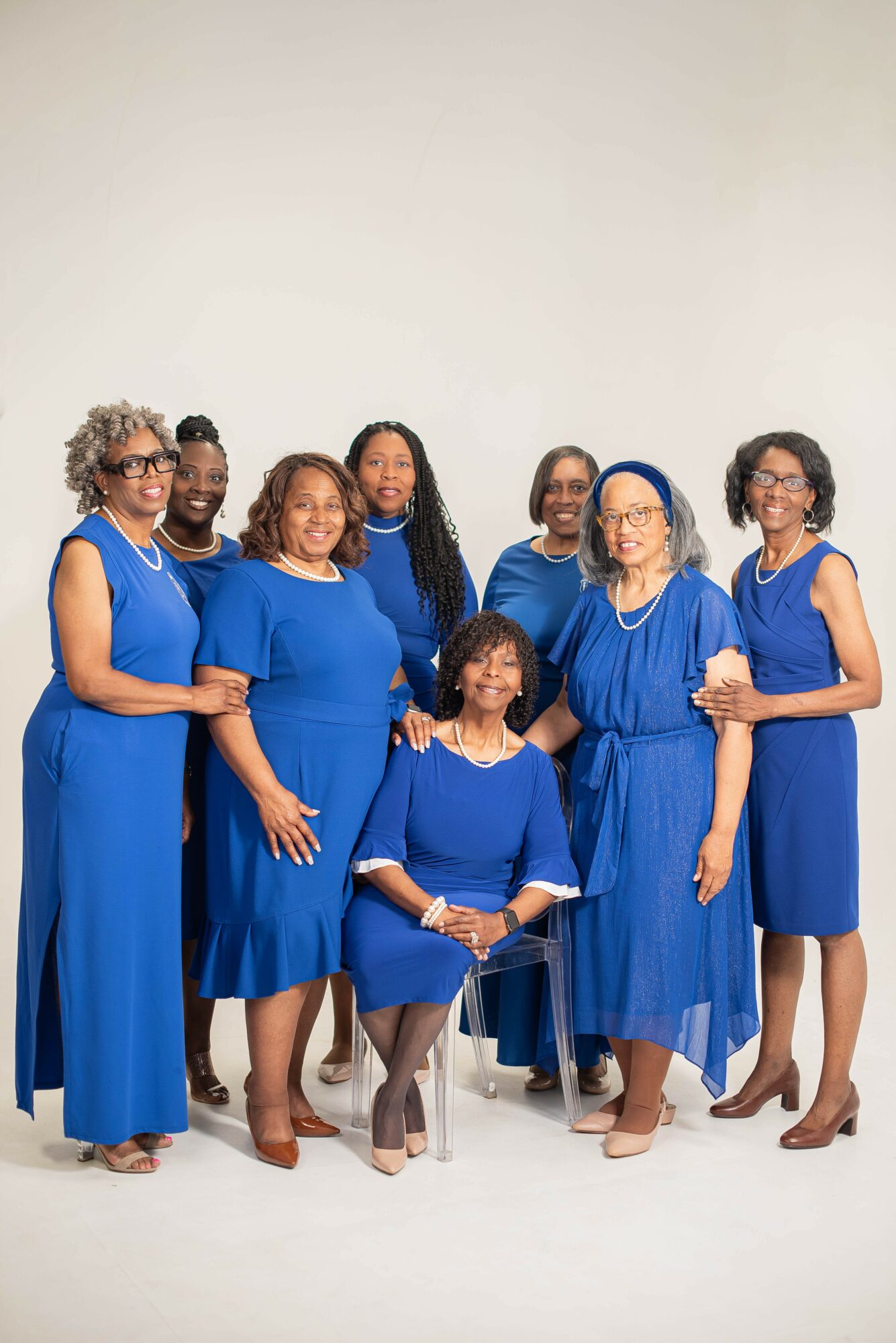 Group of eight women in blue dresses posing together against a plain white background.