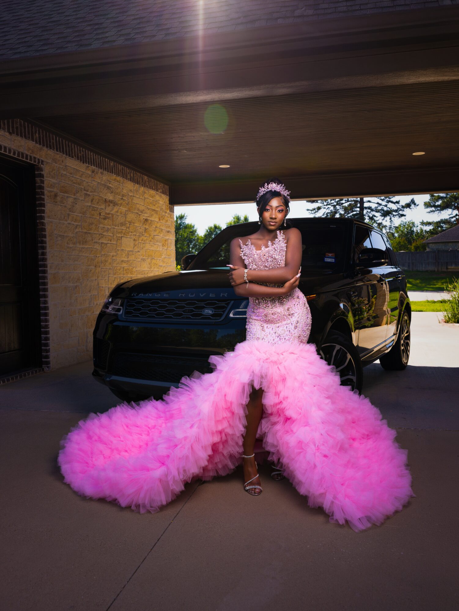 Young woman in a pink dress with a large fluffy pink train, standing outdoors in front of a black vehicle.