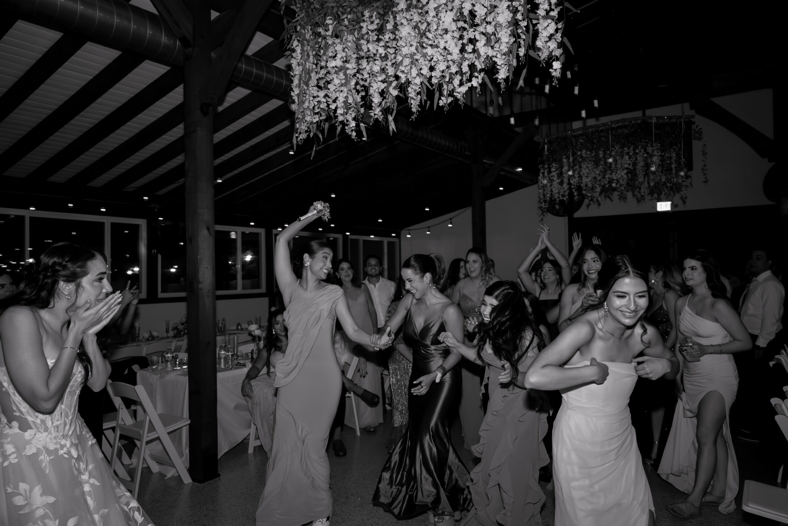 People dancing and celebrating indoors with hanging decorations and chandeliers, some clapping and smiling, in a festive setting.