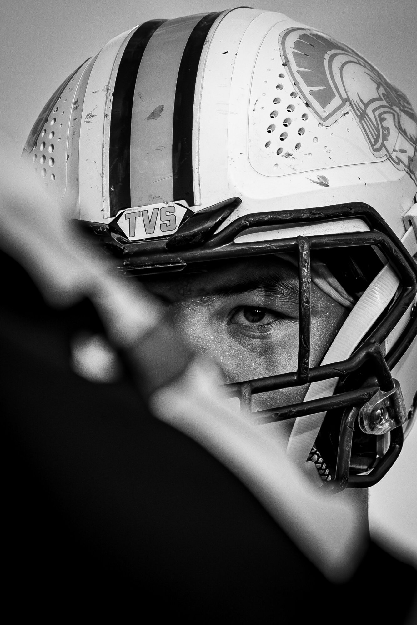 Close-up of a football player wearing a helmet with a faceguard, focusing on one eye, in black and white.