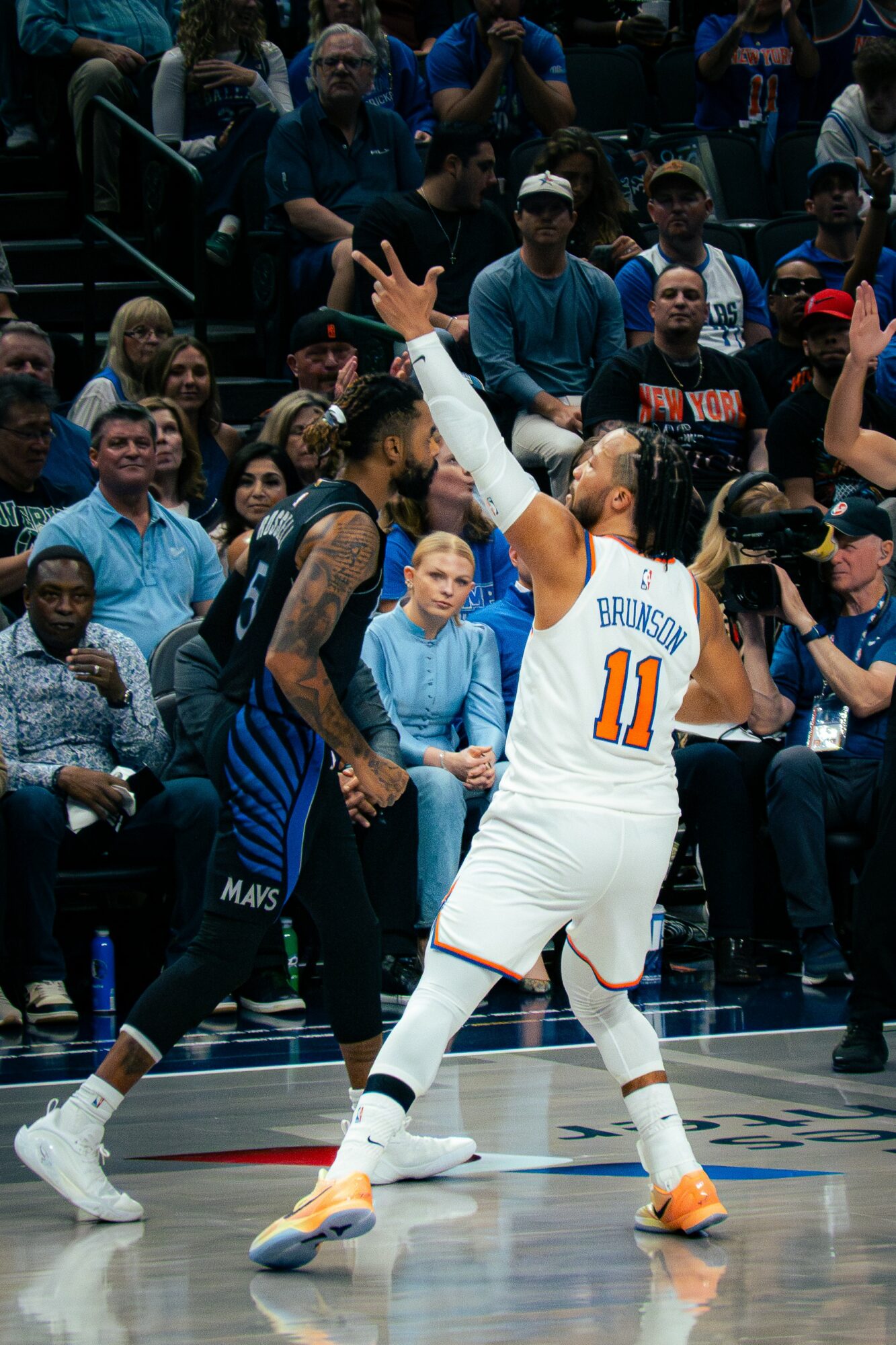 Basketball player in white jersey with number 11 raises arm during game, crowd seated in background.