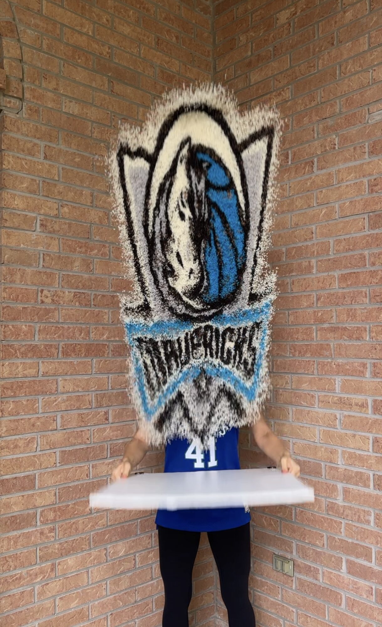 Person holding a tray in front of a brick wall with a large sports team logo and the number 41.
