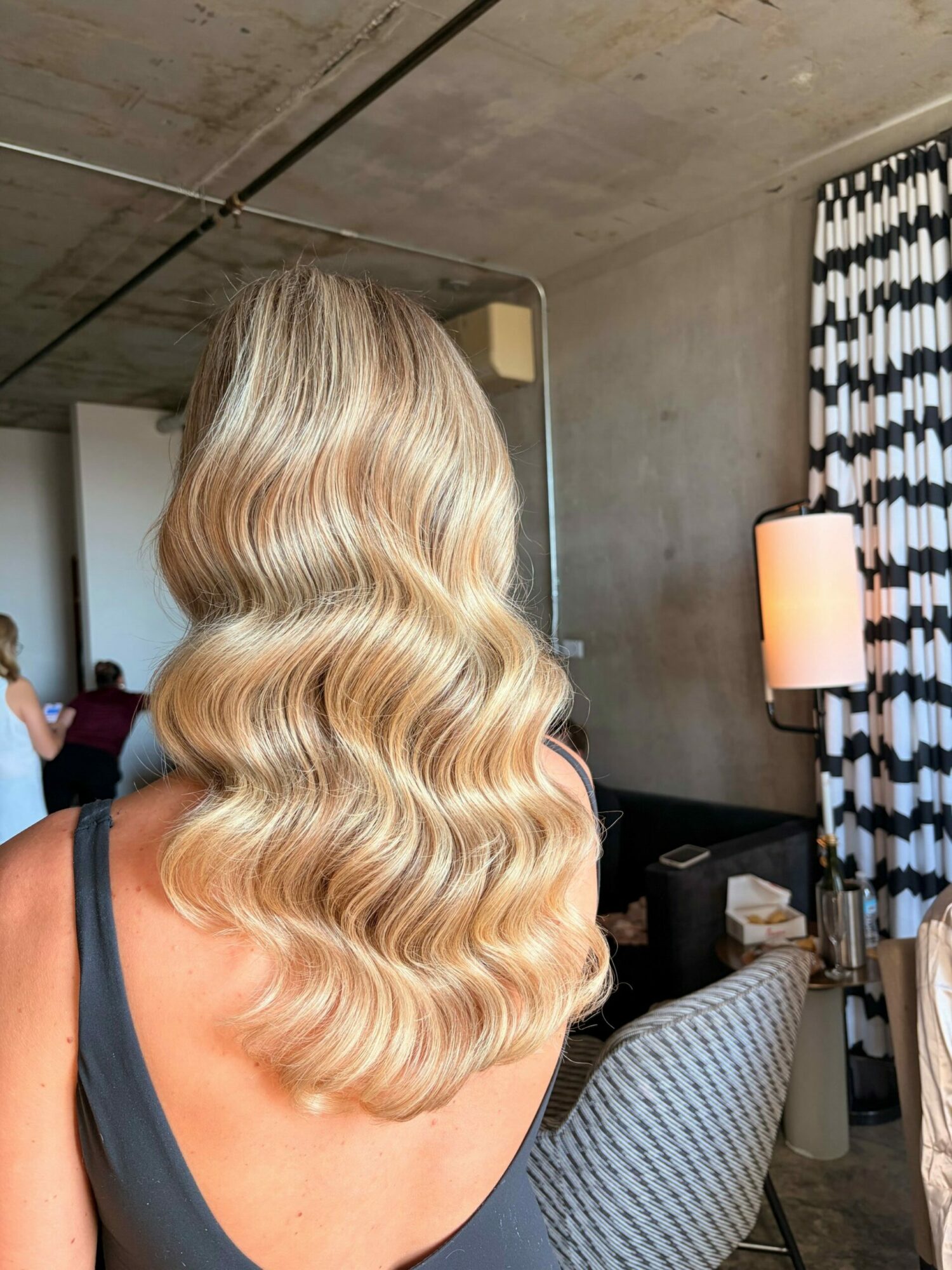 Side view of a woman with long, wavy blonde hair in a salon, facing away from the camera.