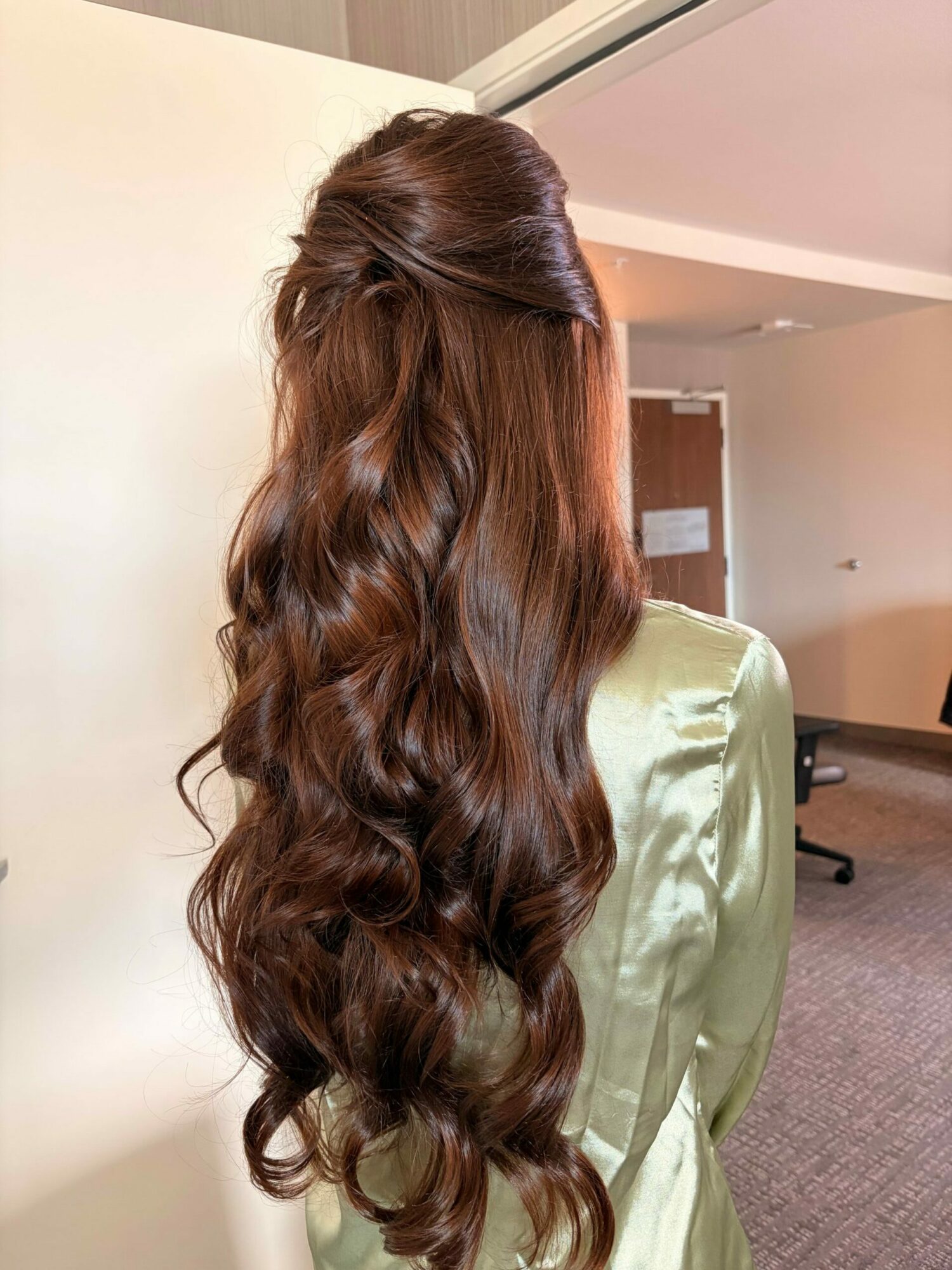 Long, wavy brown hair flowing down a person's back, with a green satin garment visible.