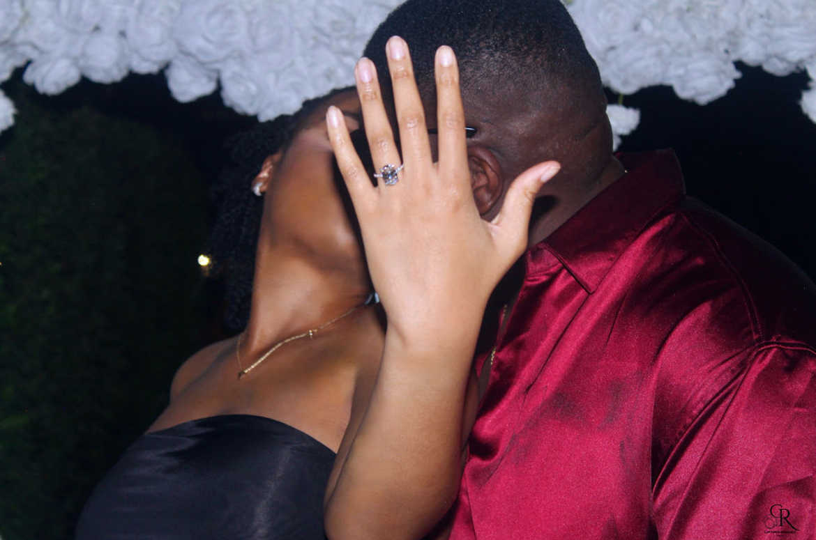 A couple kissing, woman with hand on man's face, woman wearing a black strapless dress, man in a red satin shirt.