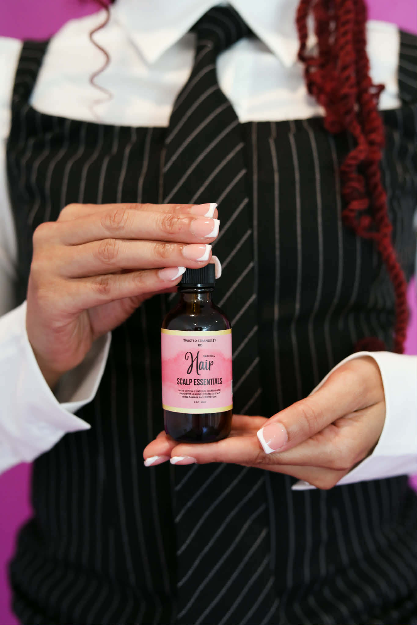 Person in striped apron holding a small bottle with a pink label, demonstrating or presenting it.