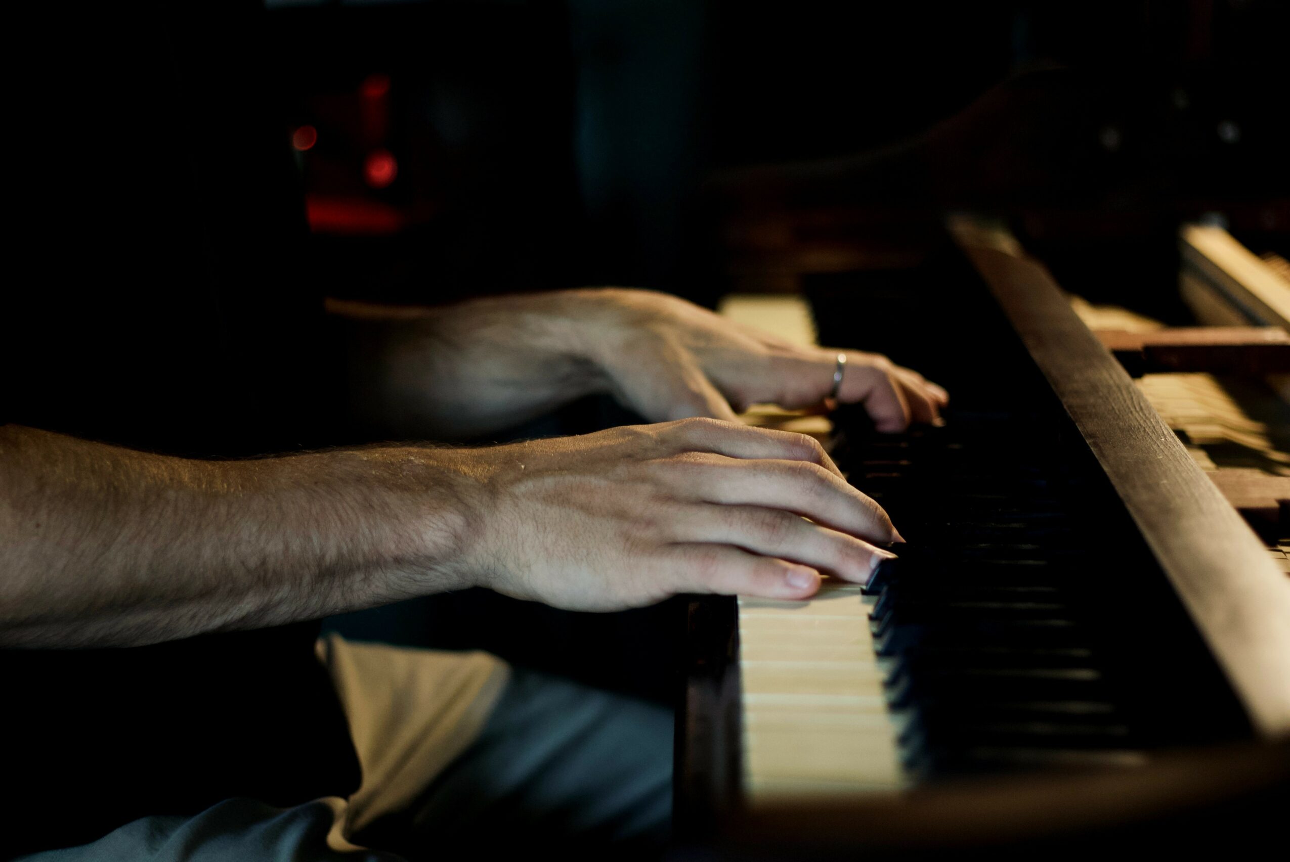 Person's hands playing piano keys in a dimly lit setting.