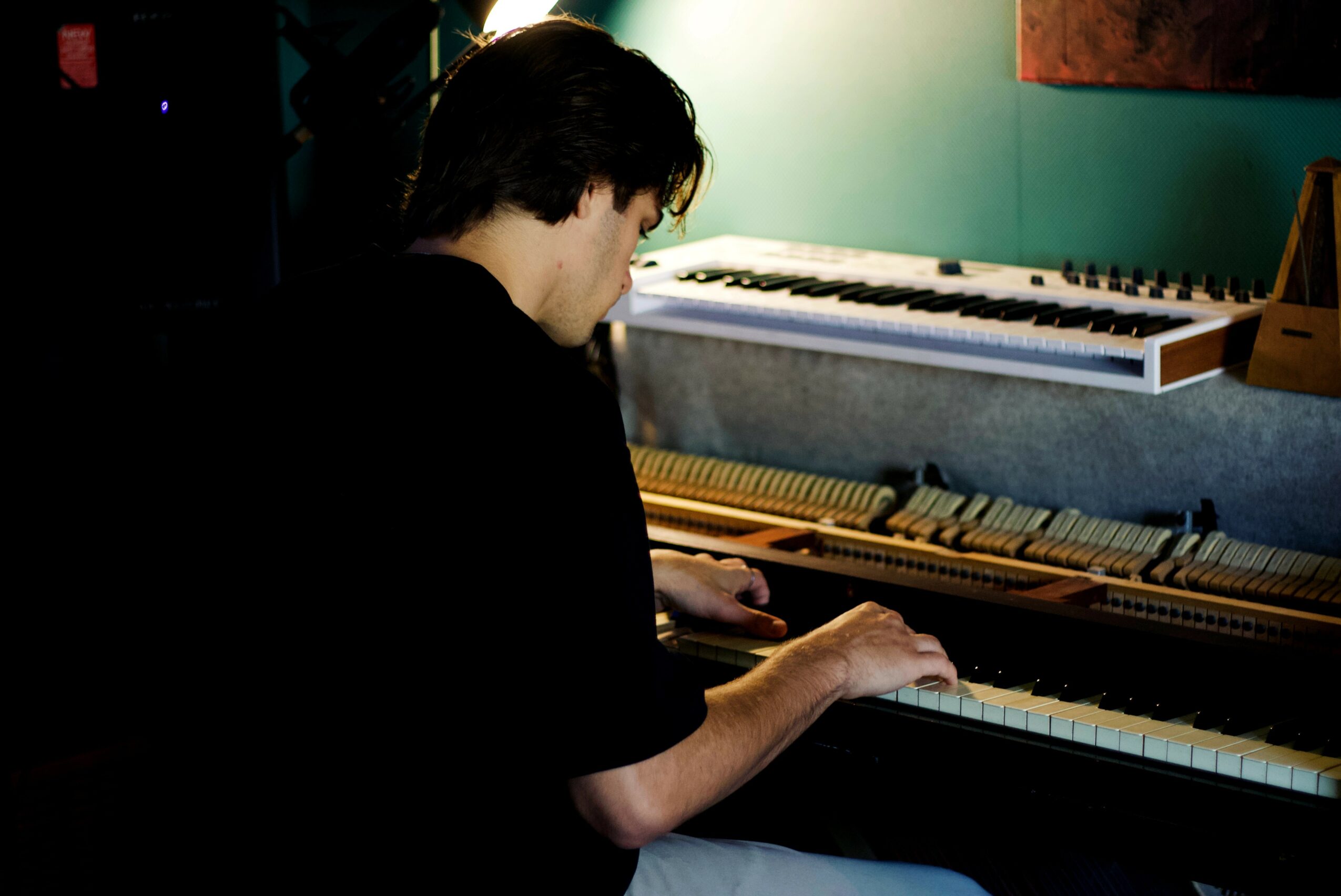 Person playing piano in a room with a keyboard on the wall behind them.