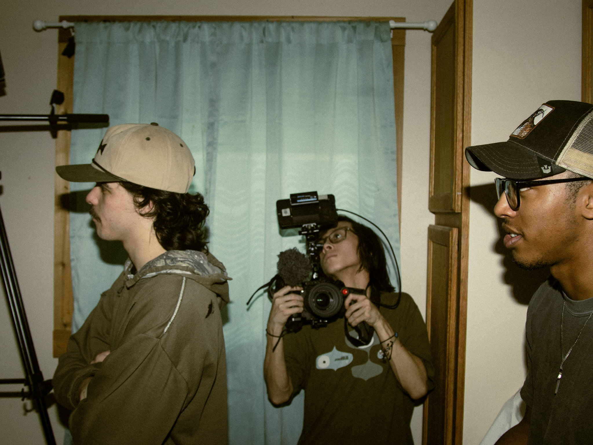 Three people in a room, one holding a camera, with a blue curtain in the background.