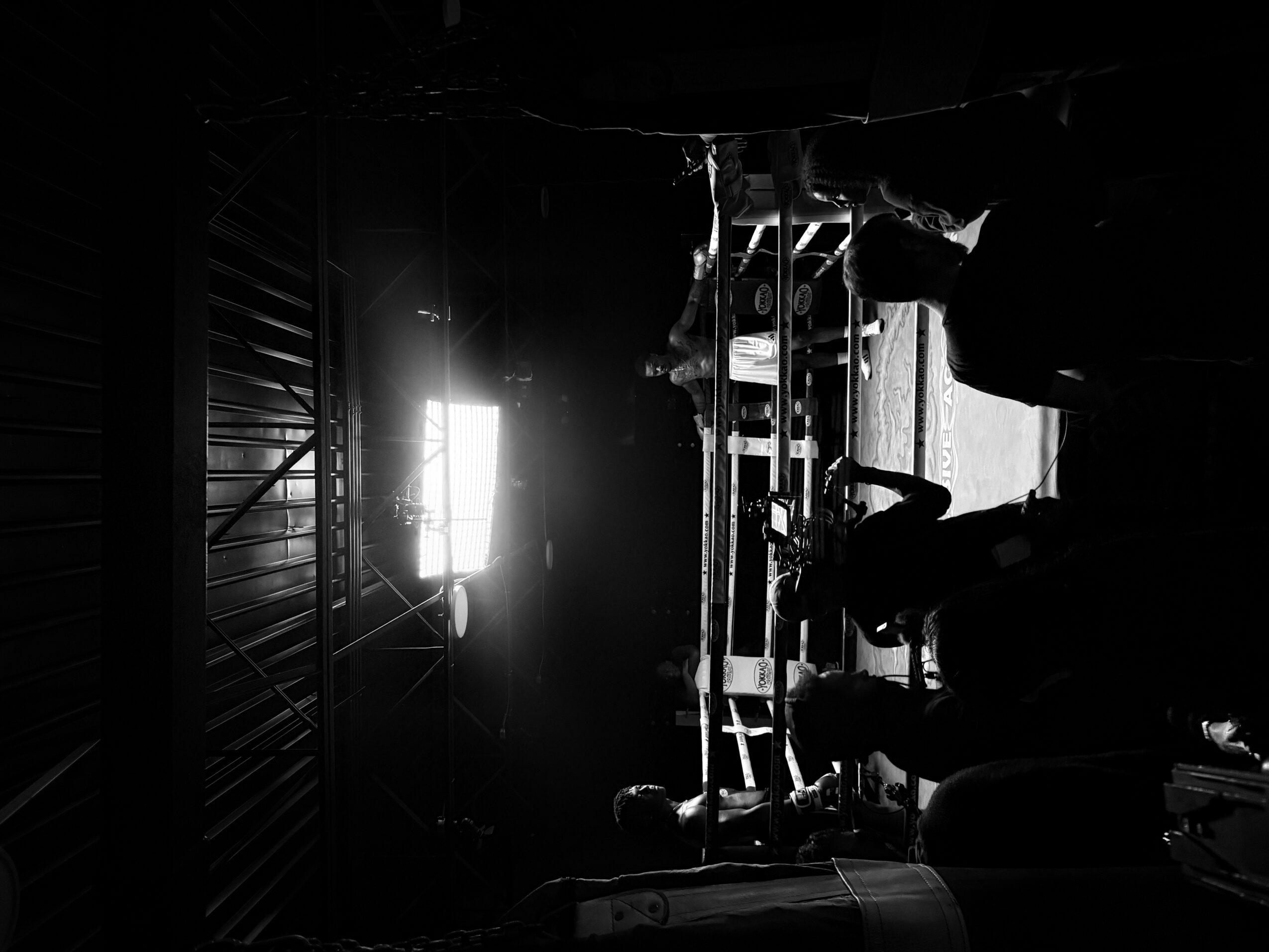 People working in a dark industrial space with a bright light source, silhouettes visible, equipment and structures present.
