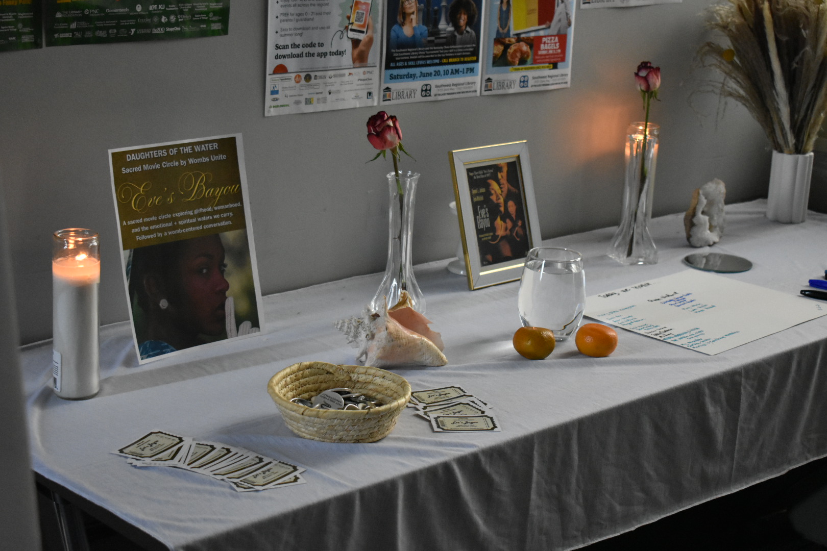 Table with candles, framed photos, flowers, and cards, covered with a white cloth, in a dimly lit room.