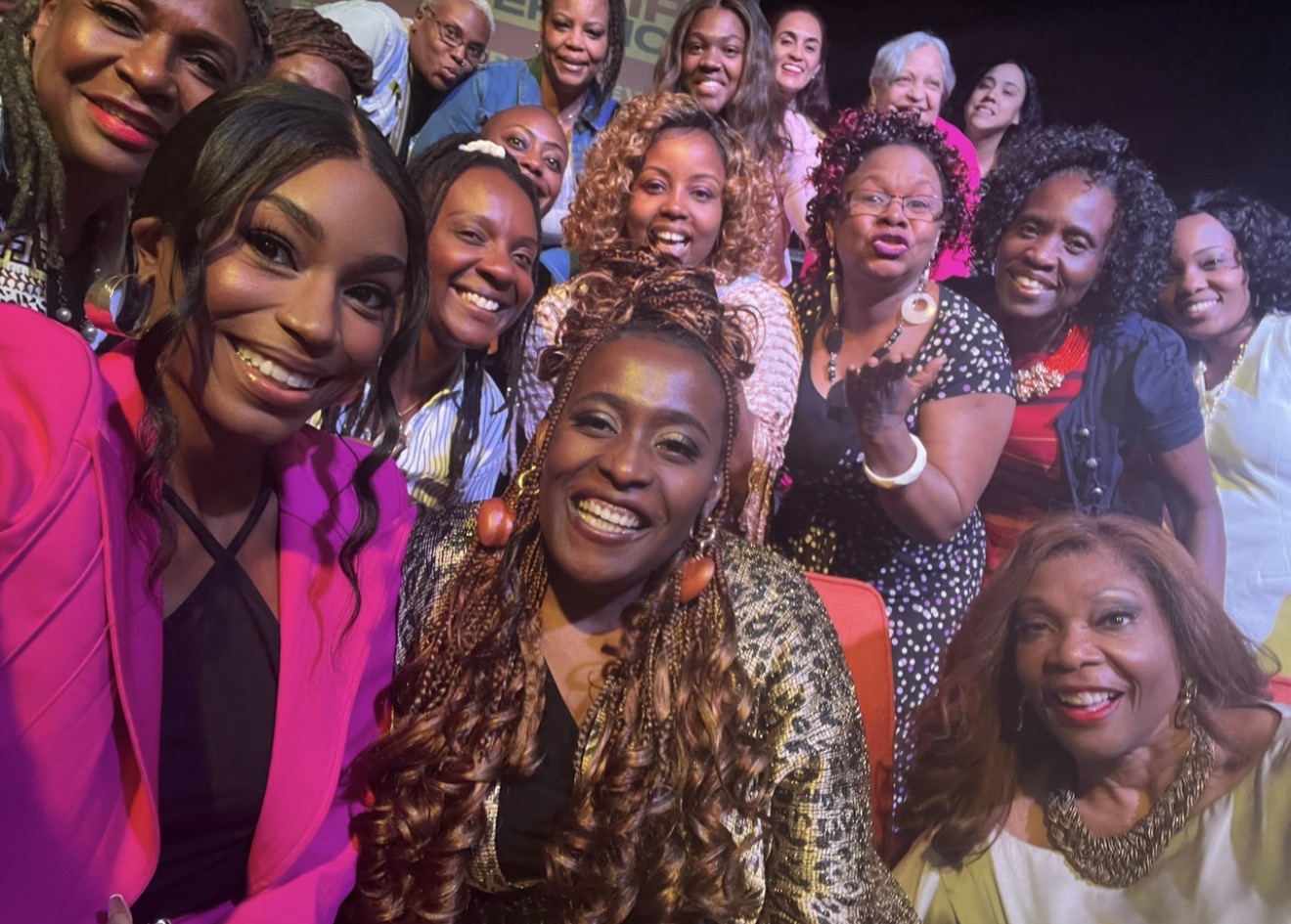 Group of women smiling and posing for a photo indoors with colorful lighting.