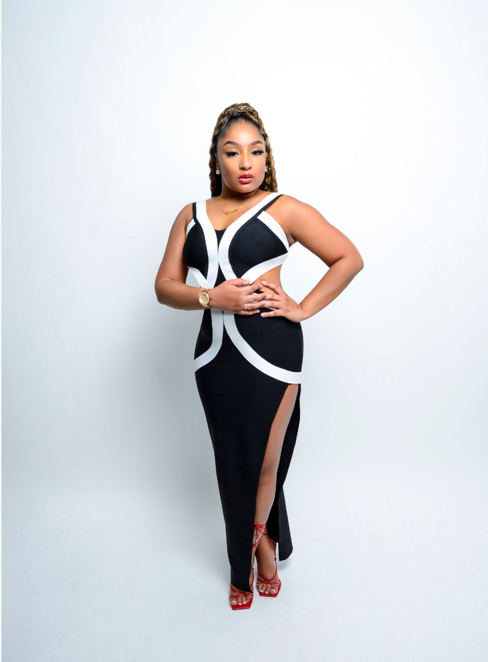 Woman in a black and white dress with a slit, standing with hands on hips, against a plain light background.