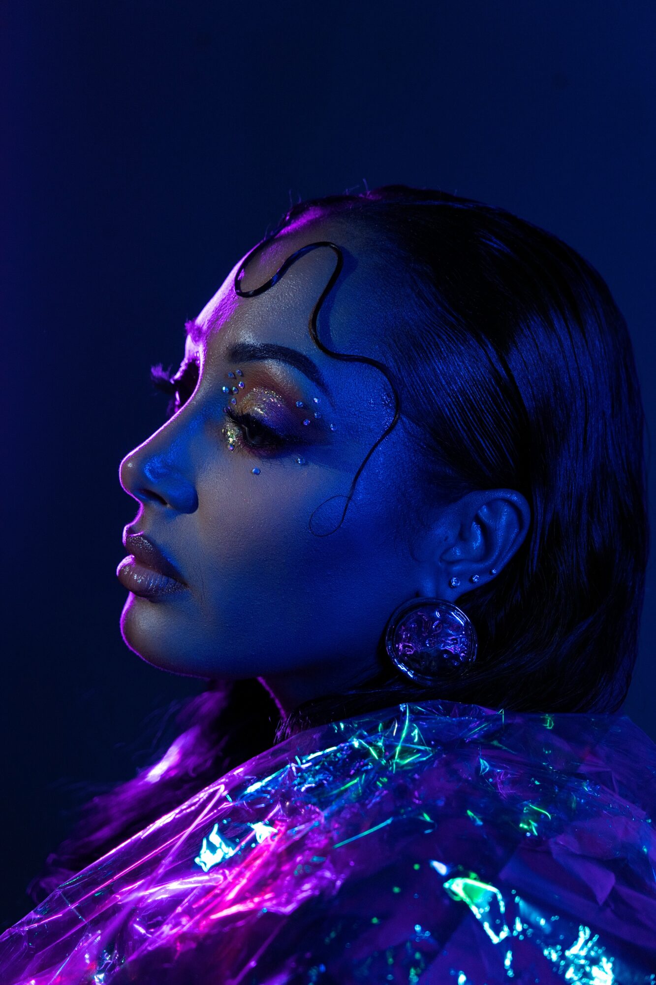 Side profile of a woman with wet hair, illuminated by blue and purple lighting, wearing shiny clothing.