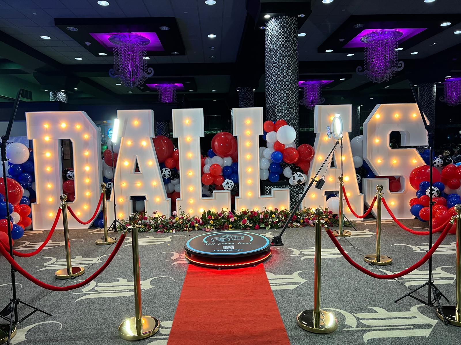 Large illuminated letters spell 'DALLAS' with balloons and a red carpet in a decorated indoor event space.