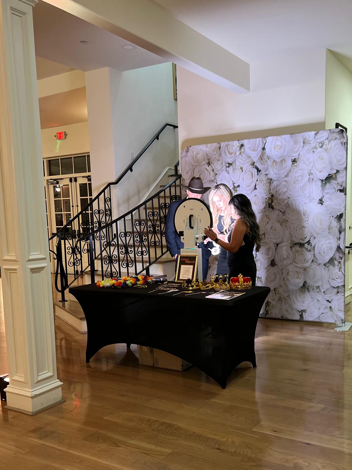 Person arranging items on a table with a large floral backdrop behind them in an indoor space.