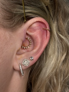 Close-up of a person's ear with multiple earrings, including a gold hoop, a diamond stud, and a curved bar, with hair partially visible.