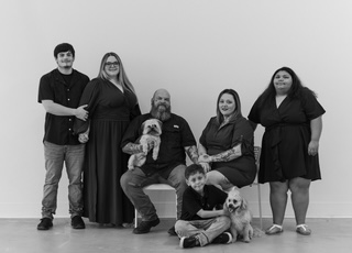Group of six people and two dogs sitting and standing against a plain wall, smiling, in black and white.