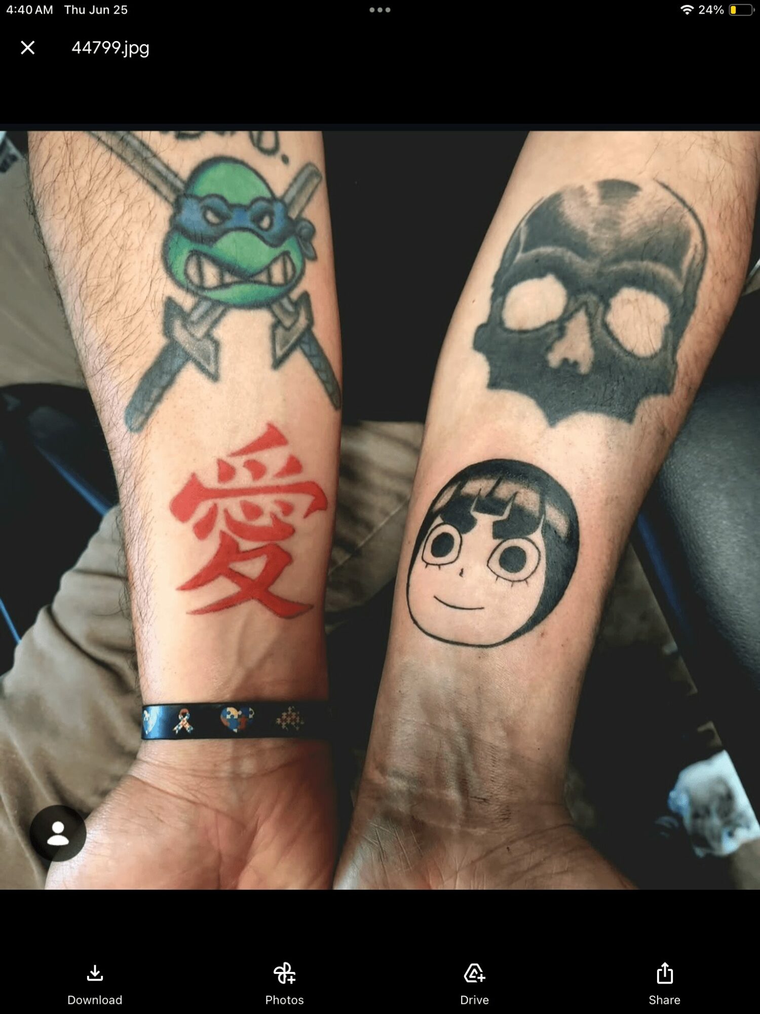Two tattoos on forearms: a green cartoon turtle with a blue mask and a red Japanese character, and a black skull with a cartoon girl face below.