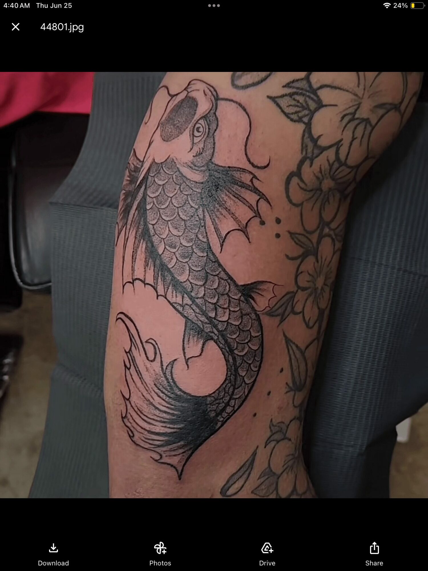 Tattoo of a fish with detailed scales and flowing fins on a person's leg, surrounded by floral designs.