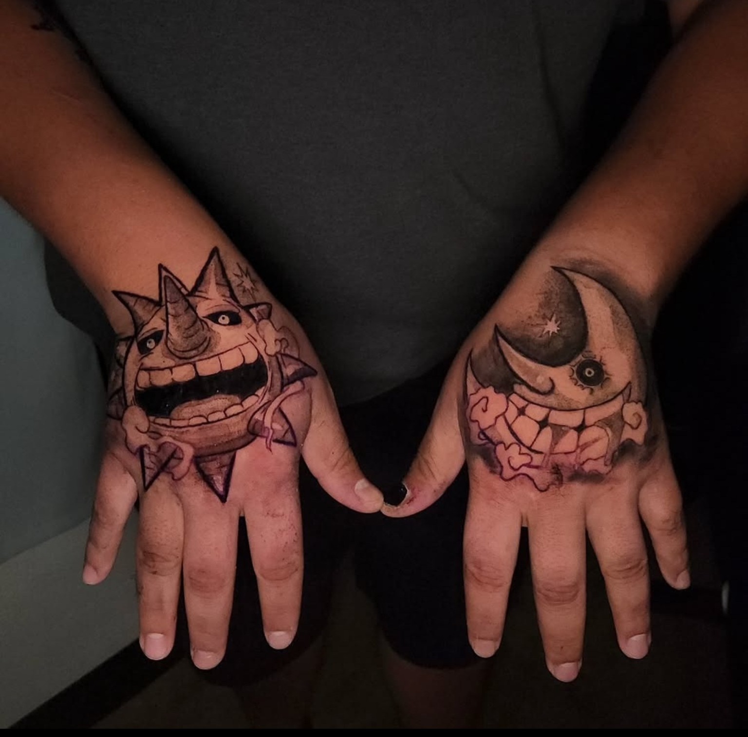 Person's hands with colorful cartoon-style tattoos of a smiling unicorn and a crescent moon with a face, fingers slightly spread.