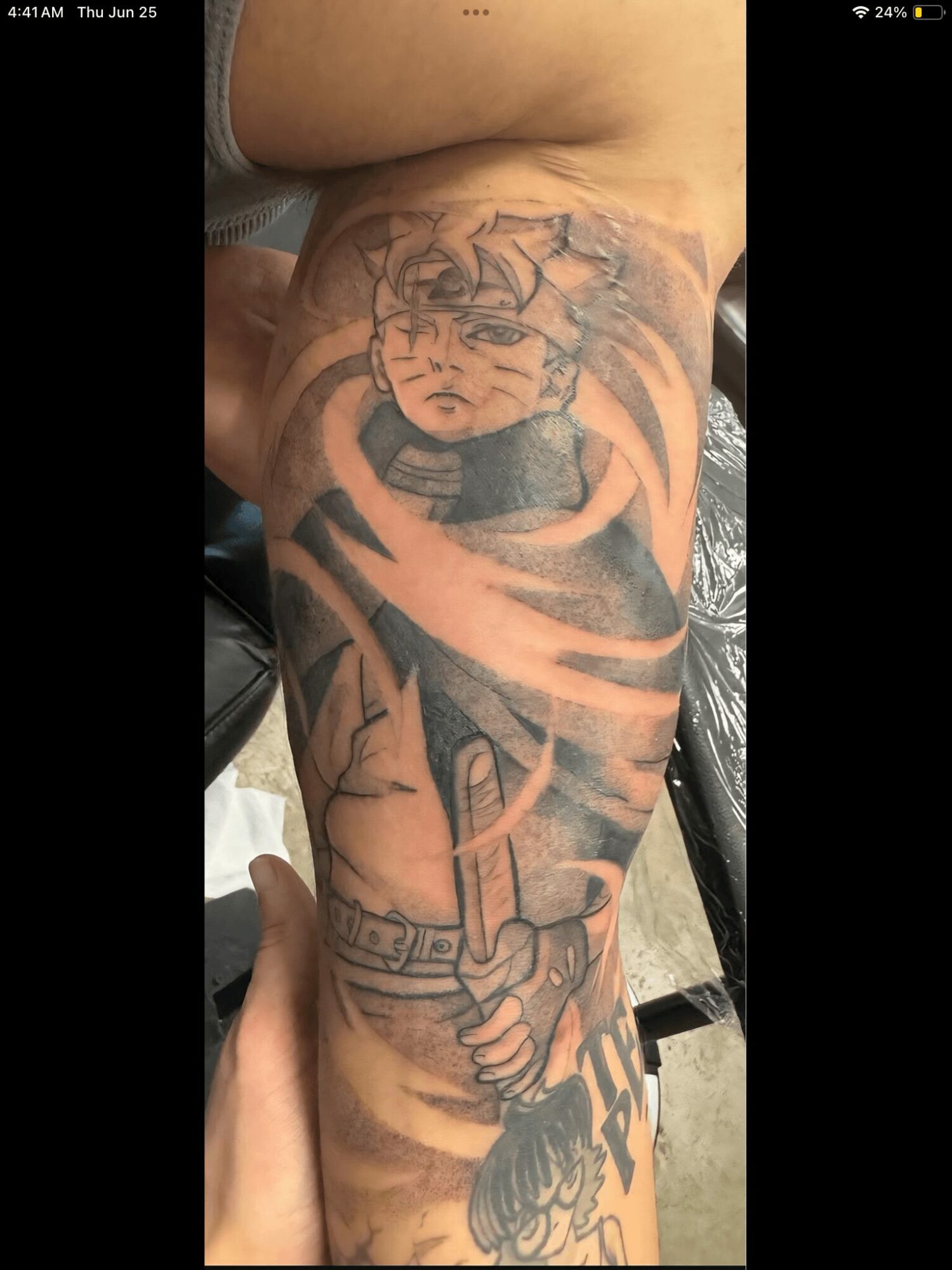 Tattoo of a cartoon character with spiky hair and a serious expression on a person's arm, holding a sword.