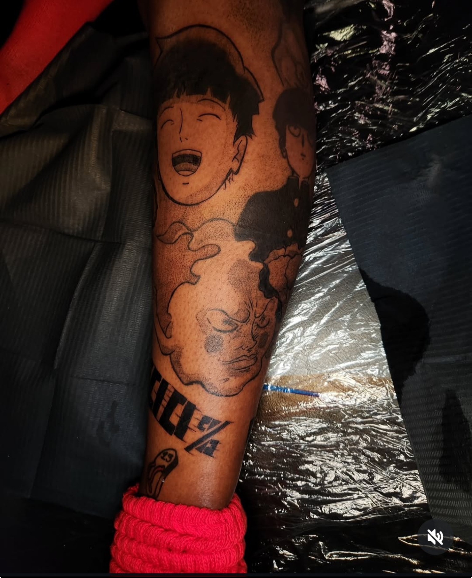 Tattoo of a smiling cartoon face with dark hair on a person's arm, with clouds and text nearby, partially covered.
