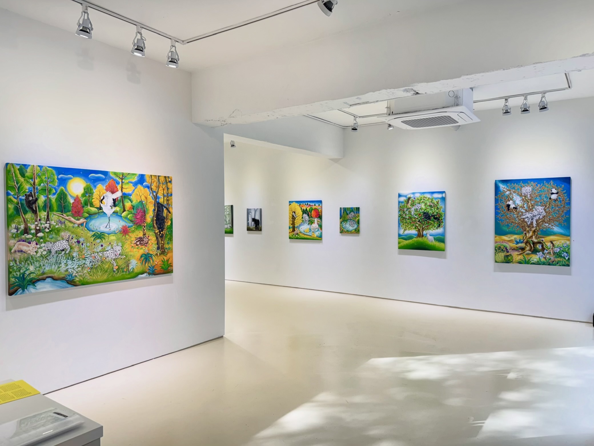 Gallery with colorful landscape paintings on white walls, bright lighting, and a polished floor.