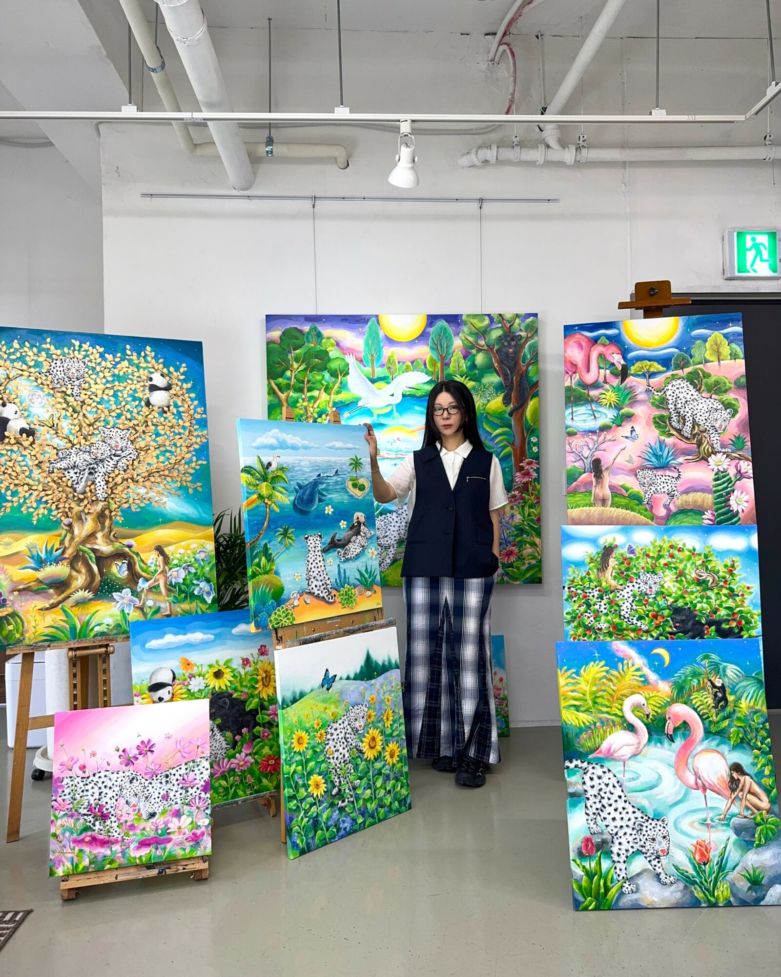 Woman standing in art gallery with colorful landscape paintings on walls and floor, white ceiling, and gray floor.
