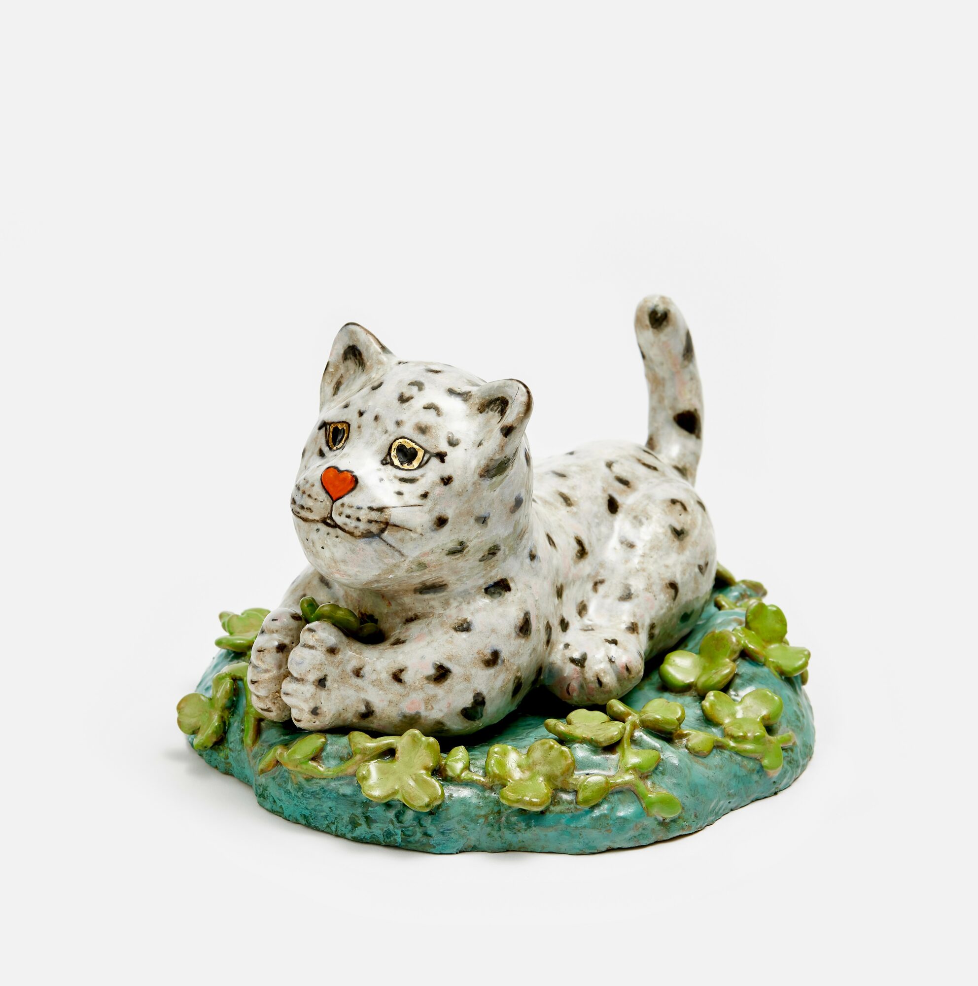 Small white leopard figurine lying on green base with yellow flowers, facing forward with tail raised, detailed spots and facial features.