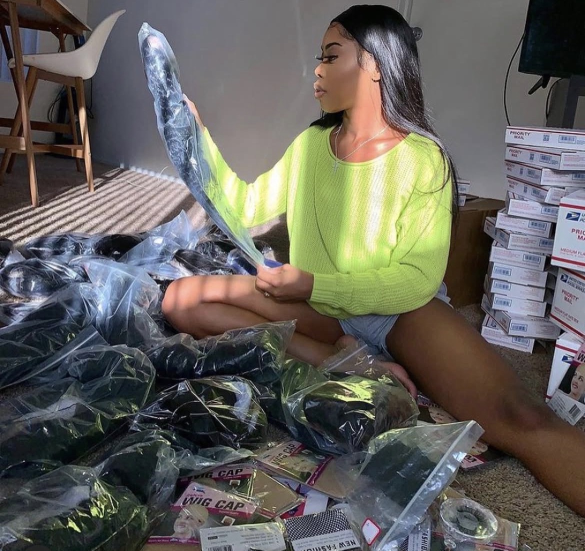 Woman sitting on the floor, surrounded by plastic bags and boxes, holding a large fish, wearing a bright green sweater.