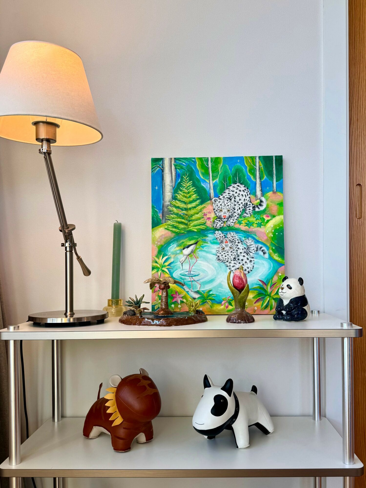 Decorative items on a white shelf include a colorful painting, a panda plush, a horse figurine, and a small plant.