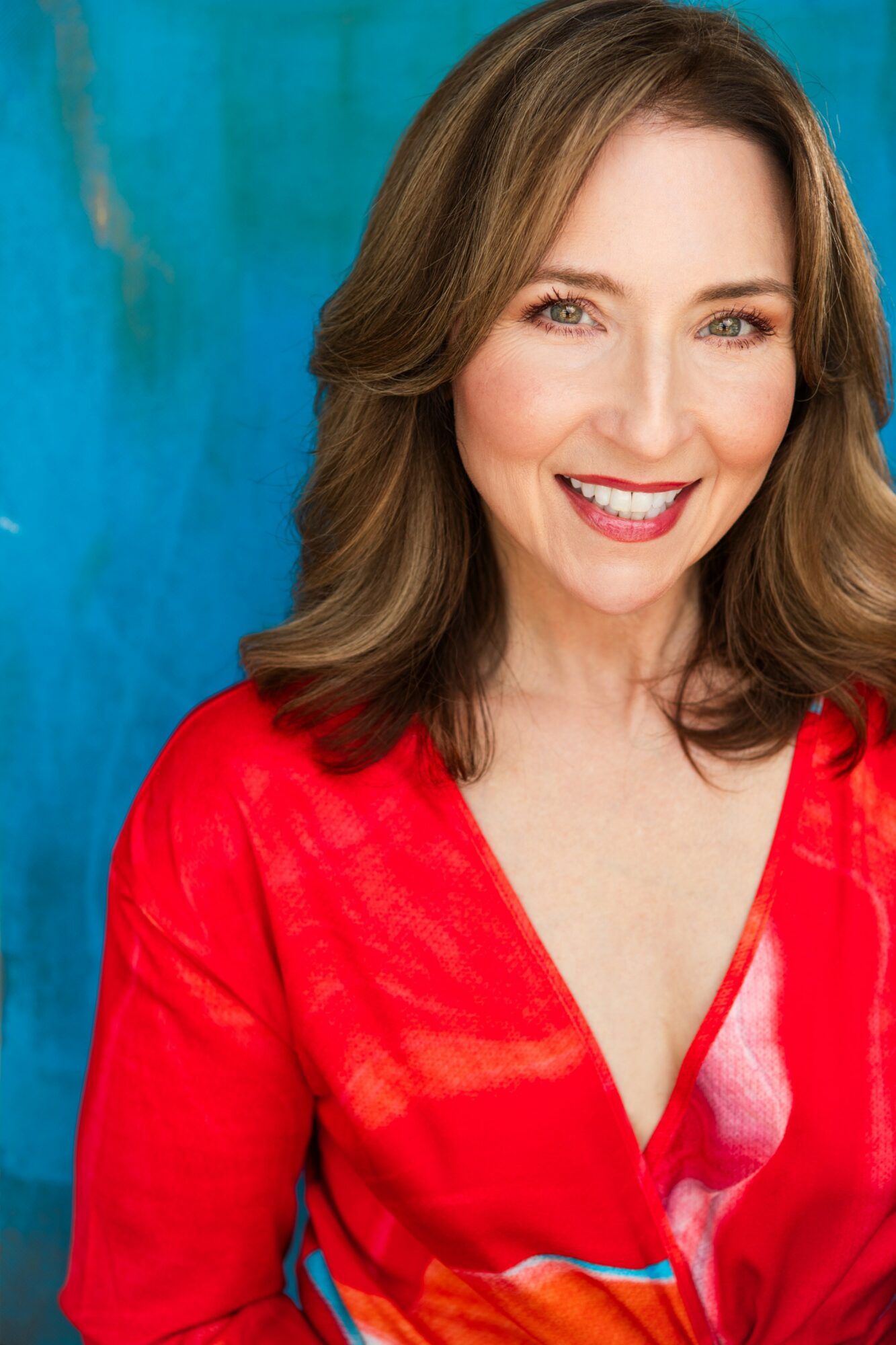 Woman with shoulder-length brown hair smiling, wearing a red top, against a blue background.