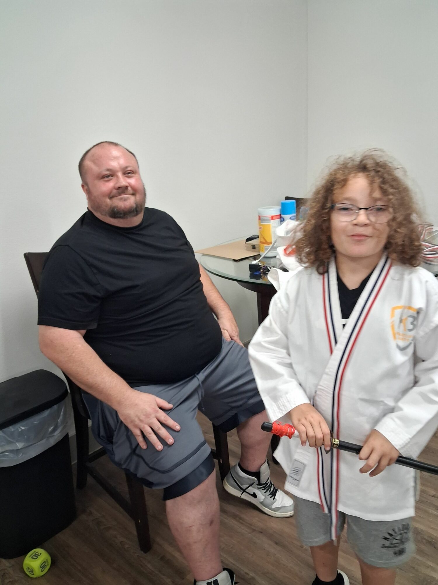 A person in a black shirt sitting on a chair with a woman in a white coat standing beside them, holding a stick.