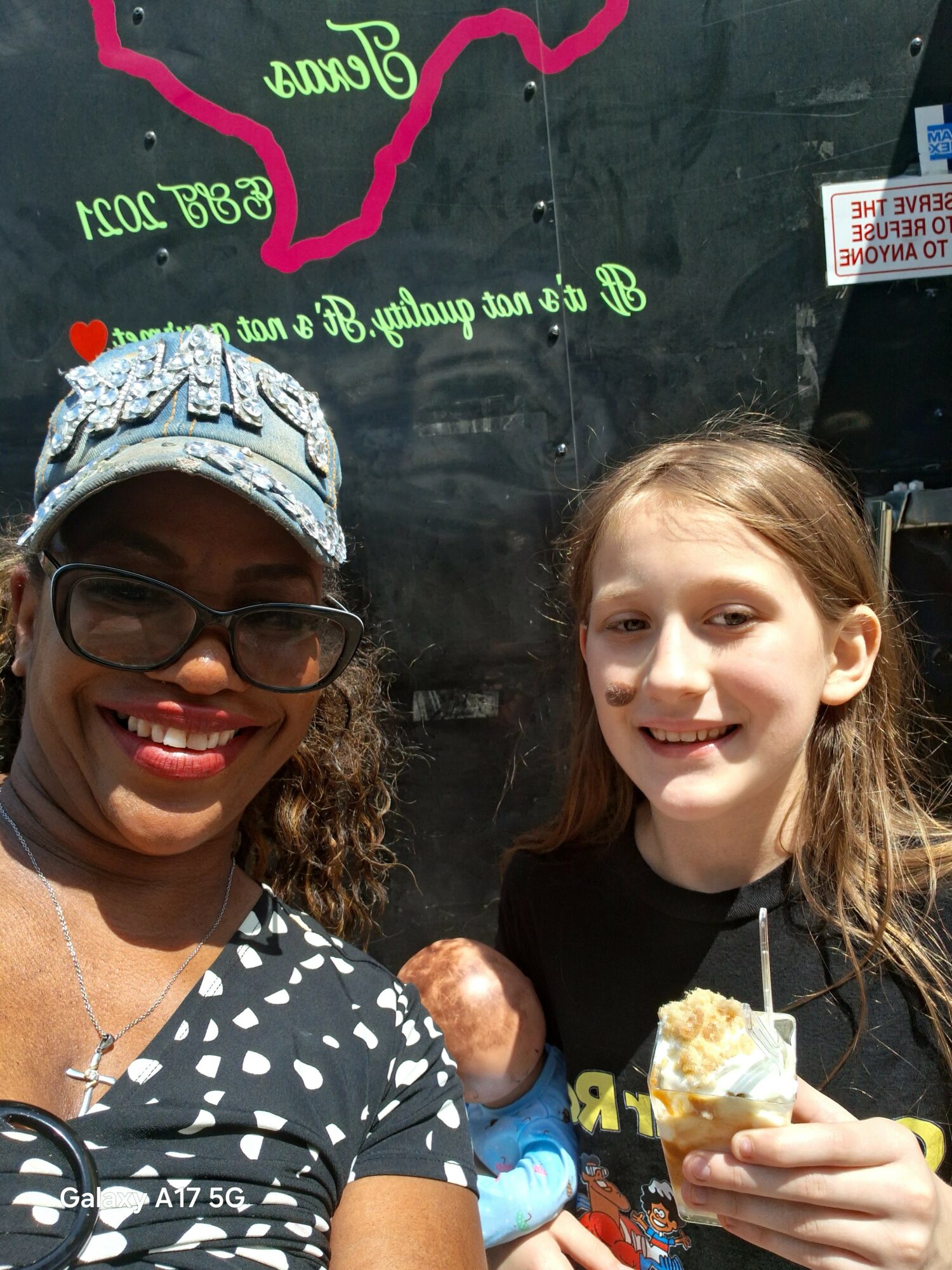 Two smiling women holding ice cream cones indoors, one wearing glasses and a patterned shirt, the other with long hair and a black shirt.