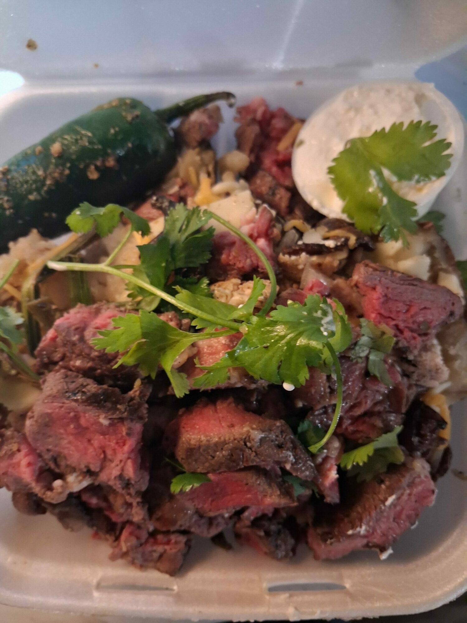 Cooked steak pieces garnished with cilantro and a slice of lime in a container.