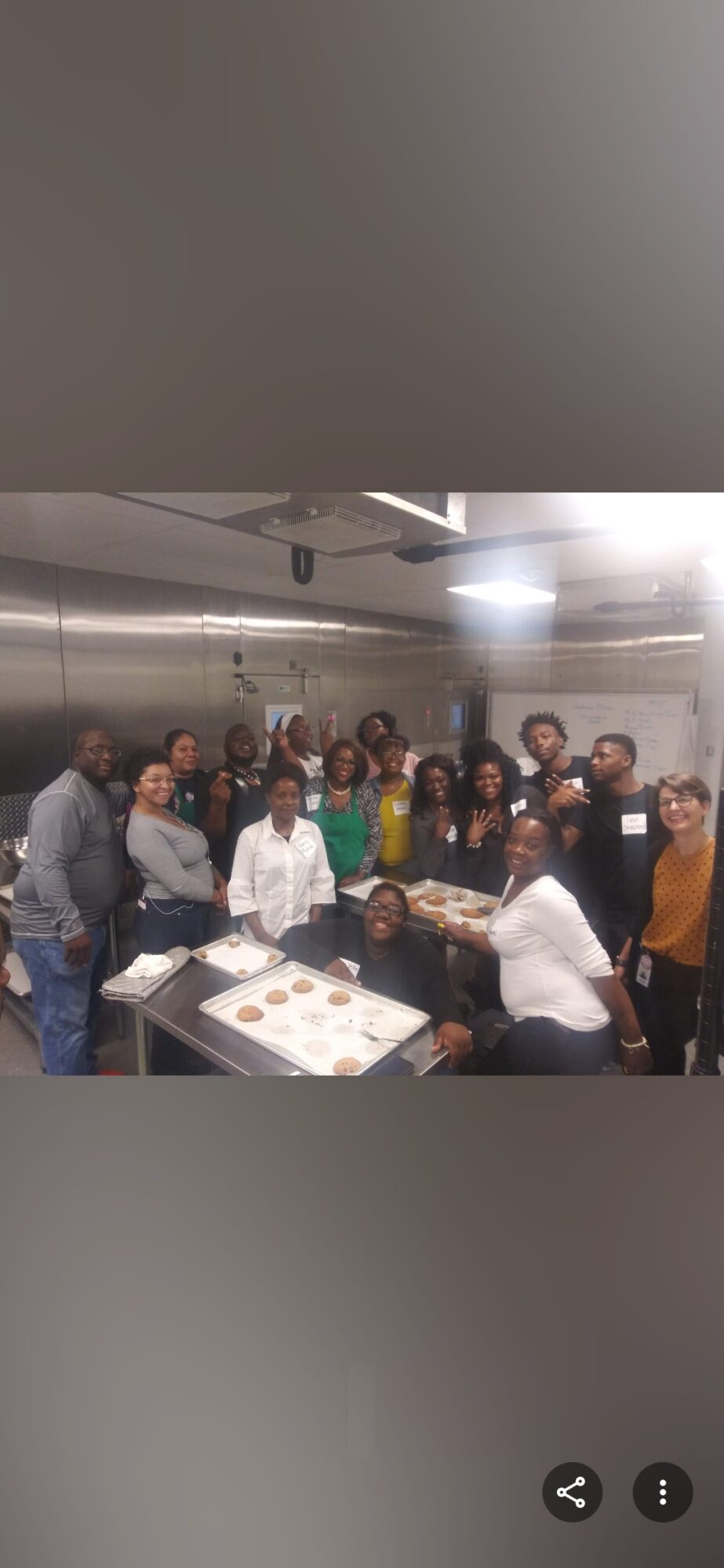Group of people gathered around a table in a kitchen, some smiling and looking at the camera.