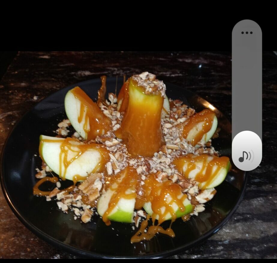 Fruit salad with orange slices, apple pieces, and shredded coconut in a black bowl on a dark surface.