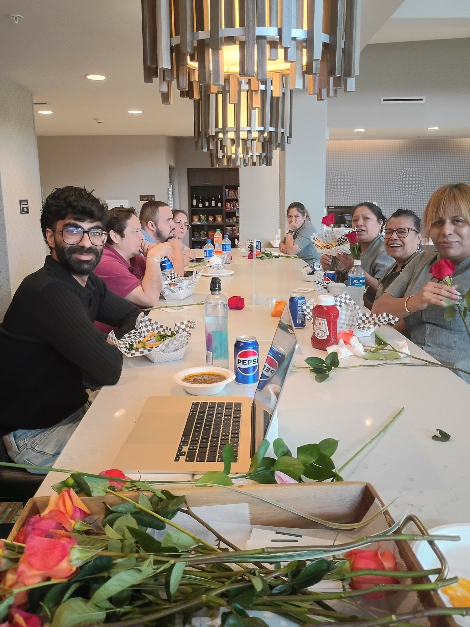 People gathered around a table with drinks and snacks, celebrating indoors with flowers and decorations.