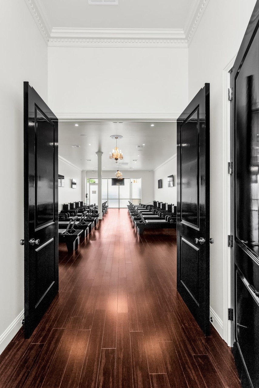 View through open black double doors into a room with rows of chairs, a chandelier, and a window at the far end.