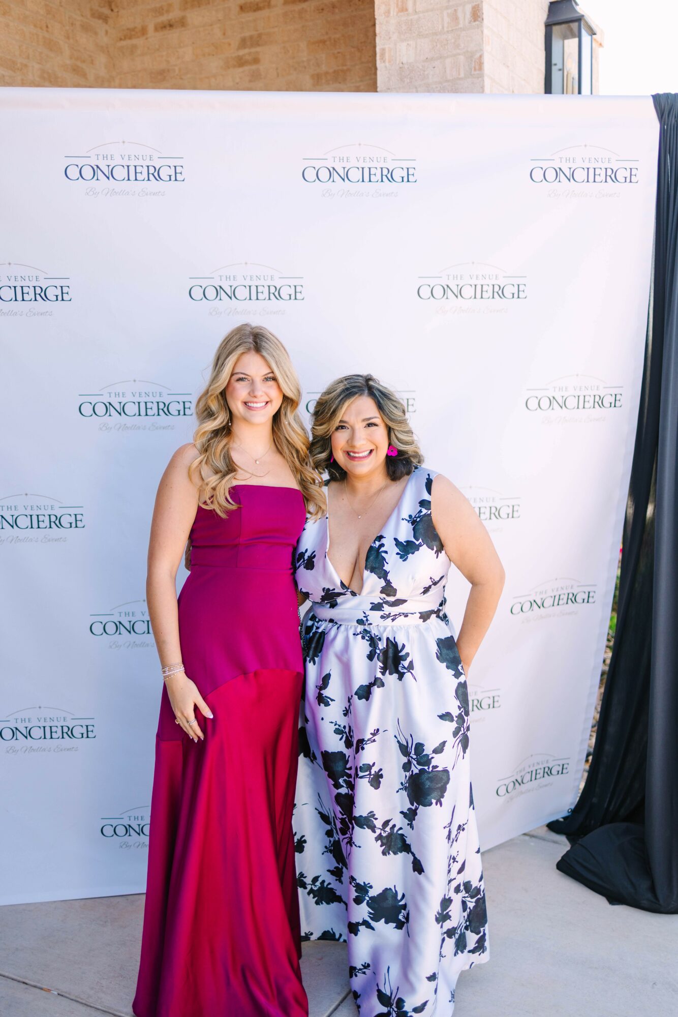Two women in elegant dresses standing in front of a backdrop with 'Concierge' logo, smiling at the camera.