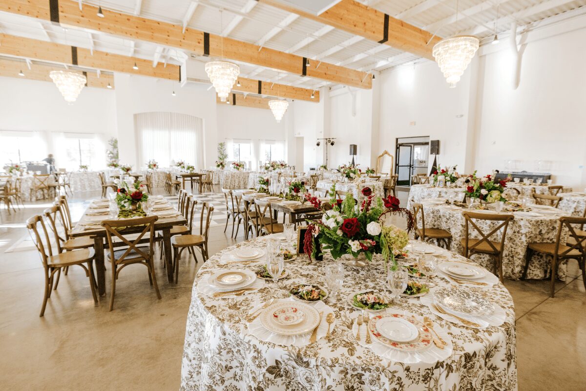 Elegant event space with decorated tables, floral centerpieces, and wooden chairs, bright with natural light and high ceilings.