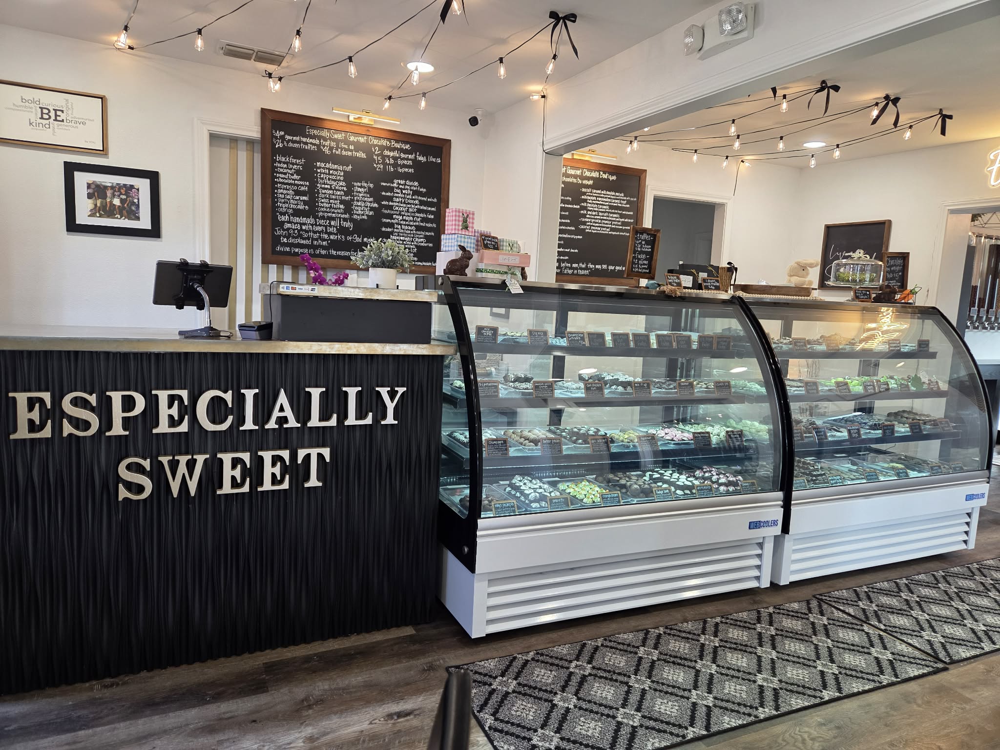 Coffee shop counter with display cases of desserts, chalkboard menus, and string lights, with a sign reading 'ESPECIALLY SWEET'.