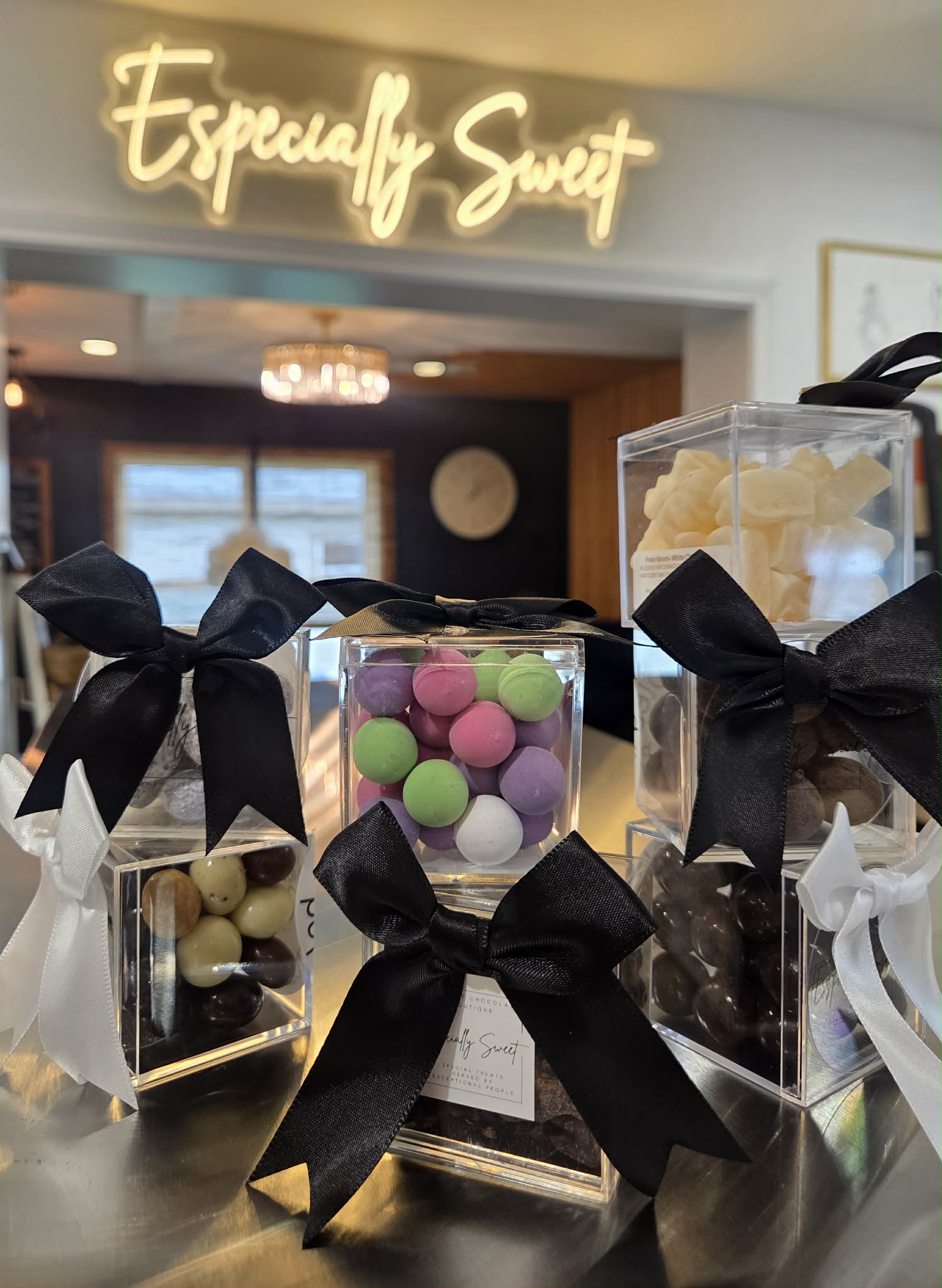 Display of colorful candies in clear containers with black ribbons, in front of a sign reading 'Especially Sweet'.