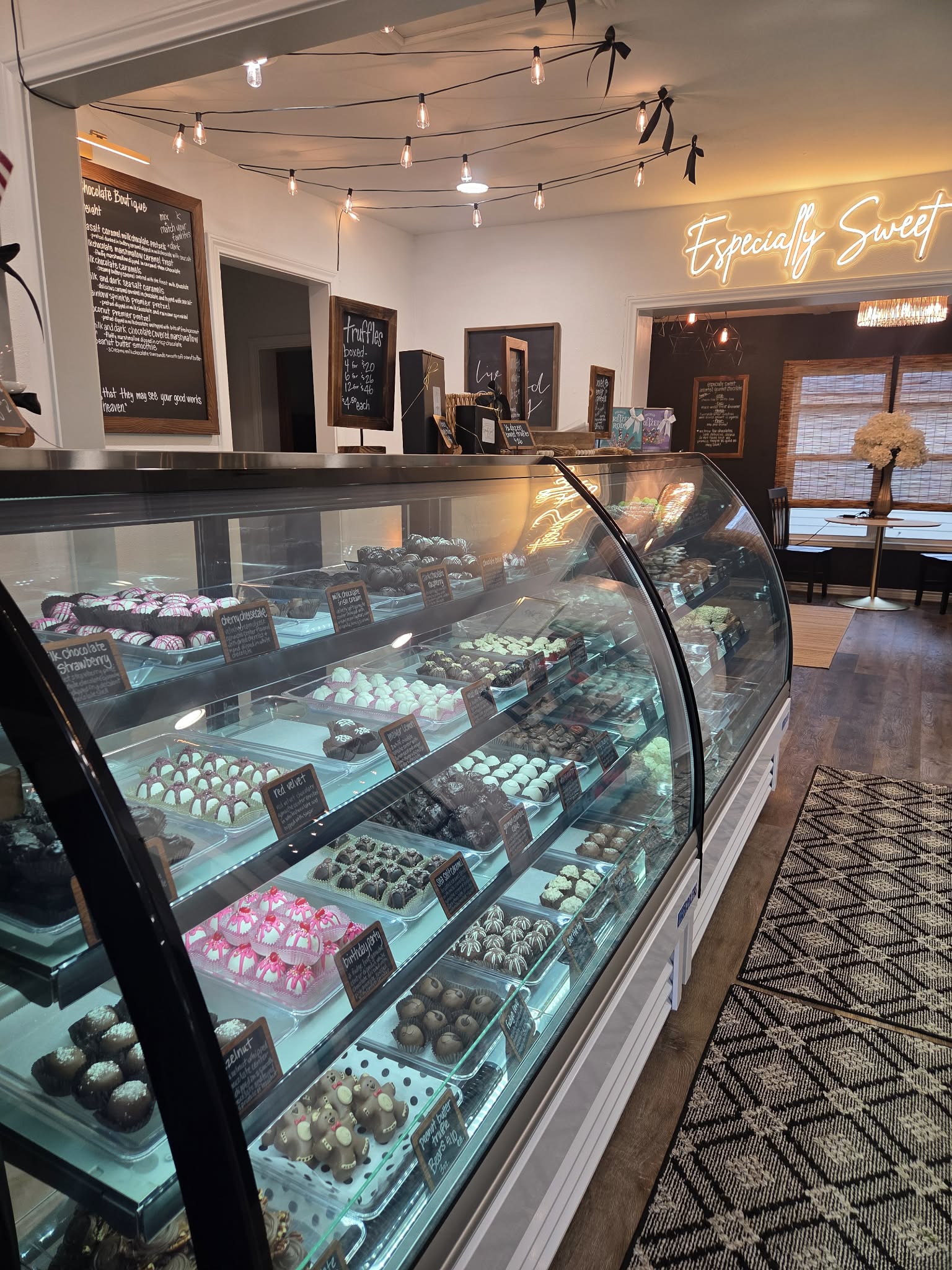 Display case filled with assorted chocolates inside a shop, with warm lighting and a neon sign in the background.