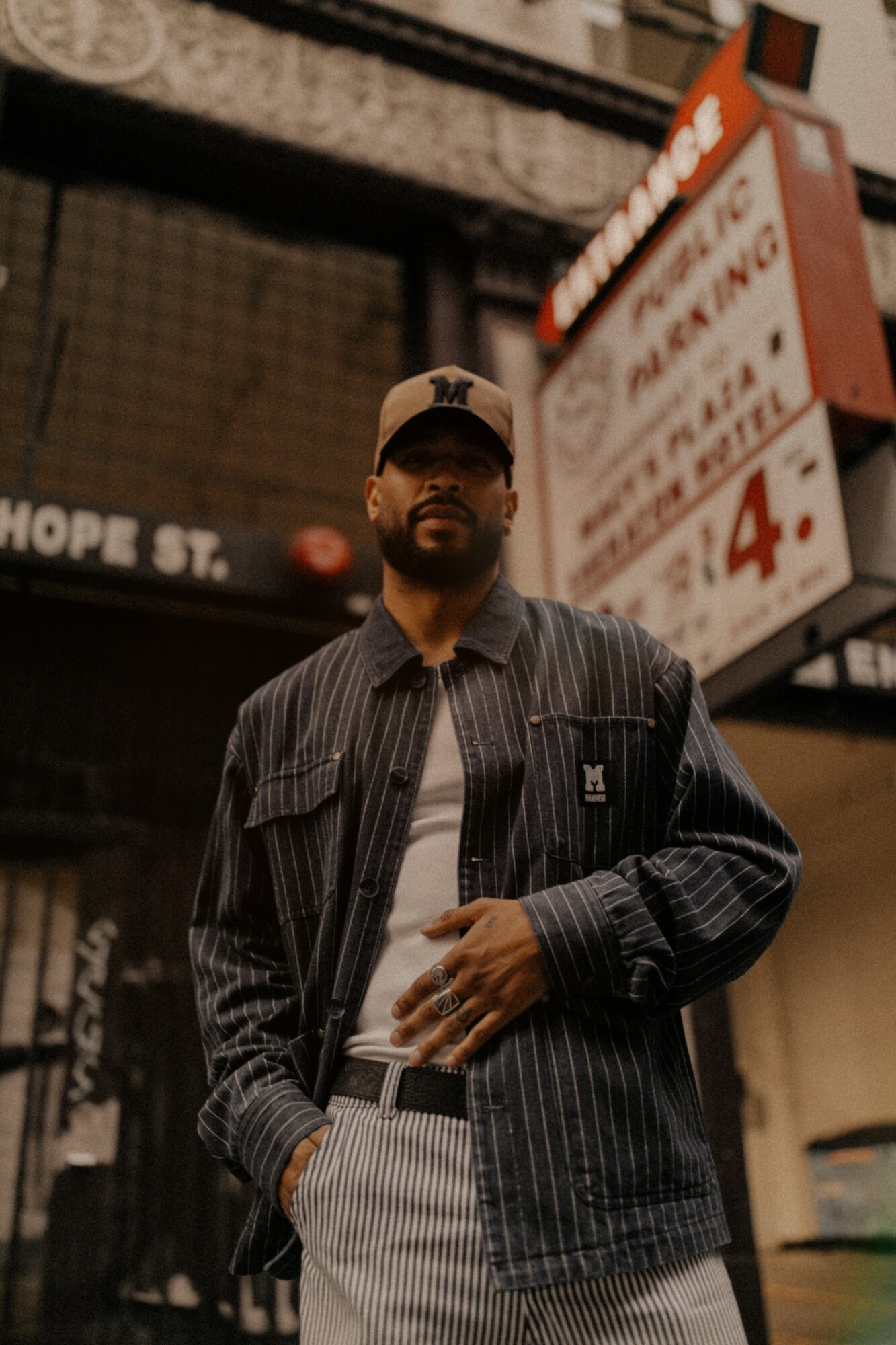 Man wearing a cap and striped jacket standing in front of a parking sign, urban background.